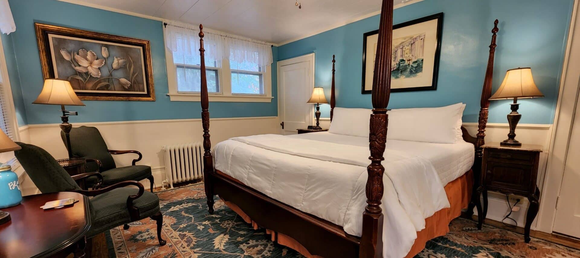 Guest room with four poster bed, side tables with lamps, and two sitting chairs