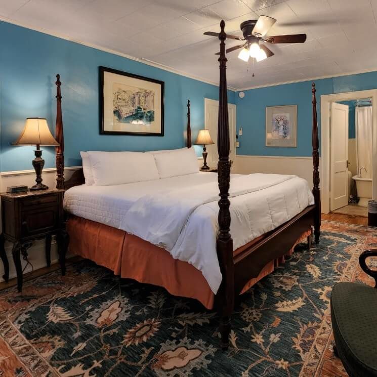 Guest room with four poster bed, sink vanity with round mirror and doorway int a bathroom