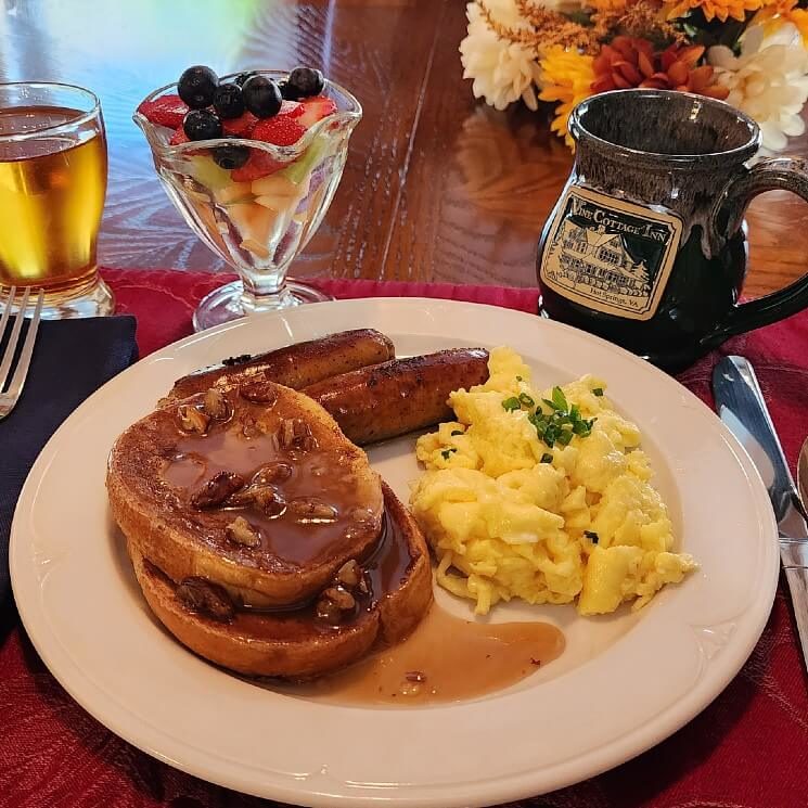 Breakfast plate of French toast, eggs, sausage and fruit, juice and ceramic coffee mug