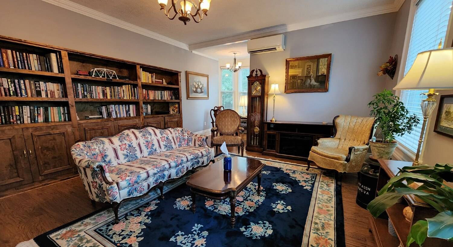 Reading room of a home with floral couch, antique chairs and wall of built-ins filled with books