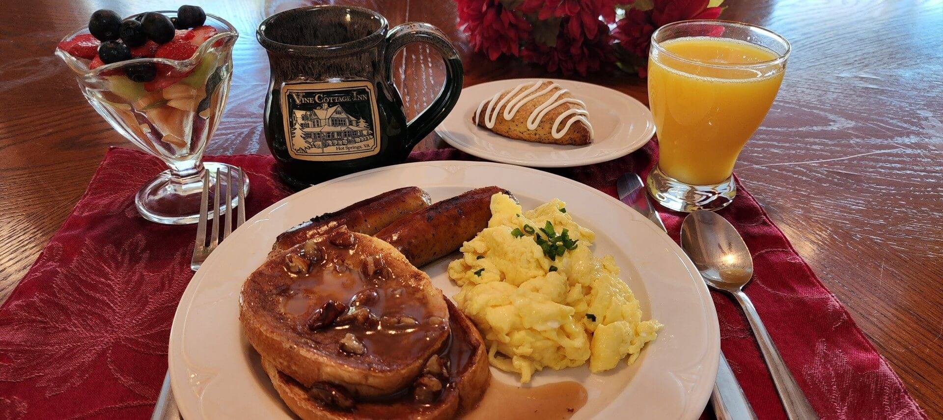 Plate of breakfast with French toast, scrambled eggs, sausage links, cup of fruit and glass of orange juice