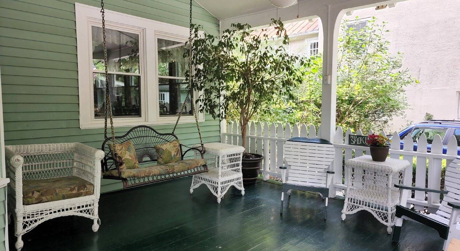 Front porch of a home with hanging swing and white wicker furniture