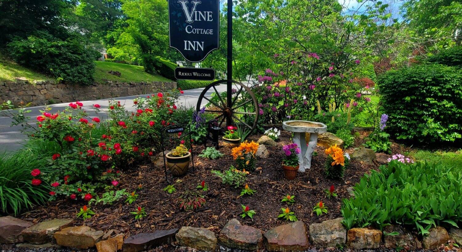 Hanging business sign with a garden area full of plants, flowers and rose bushes