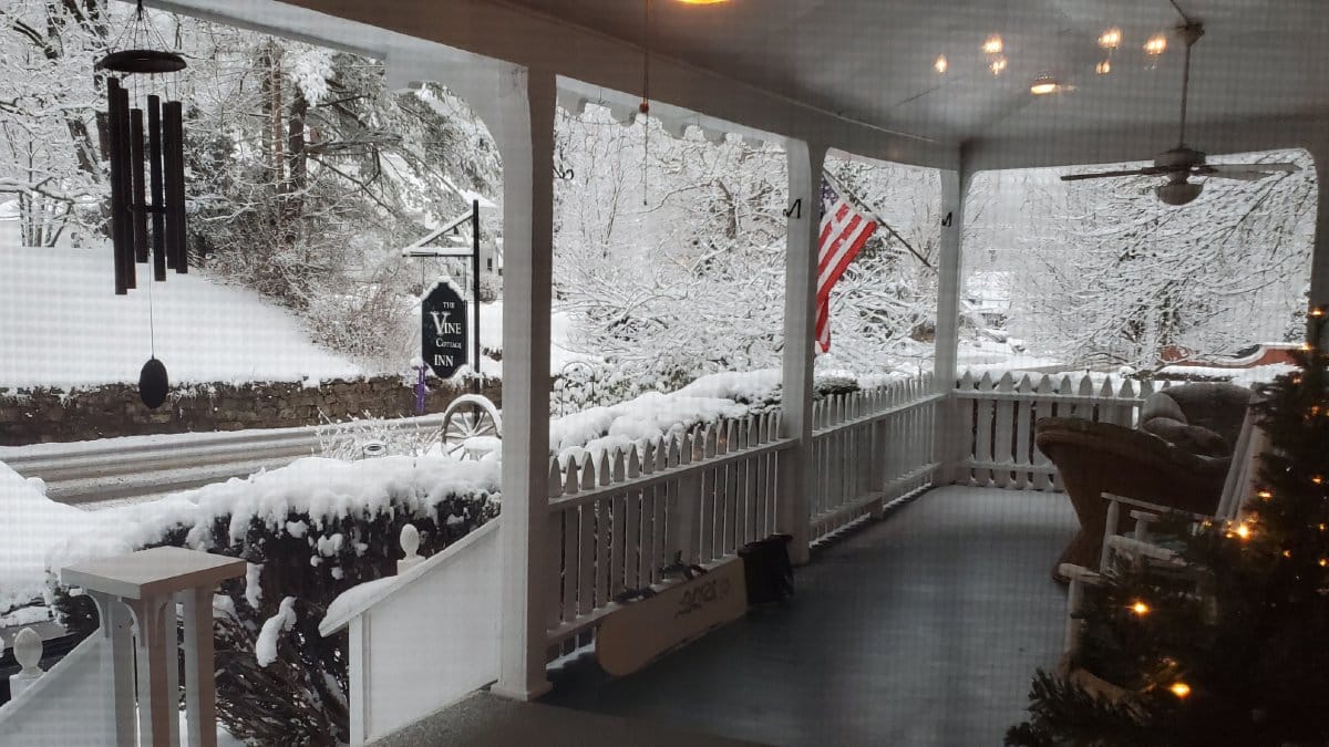 Snow-covered front porch at Vine Cottage Inn in Hot Springs, Virginia, offering a cozy winter setting.